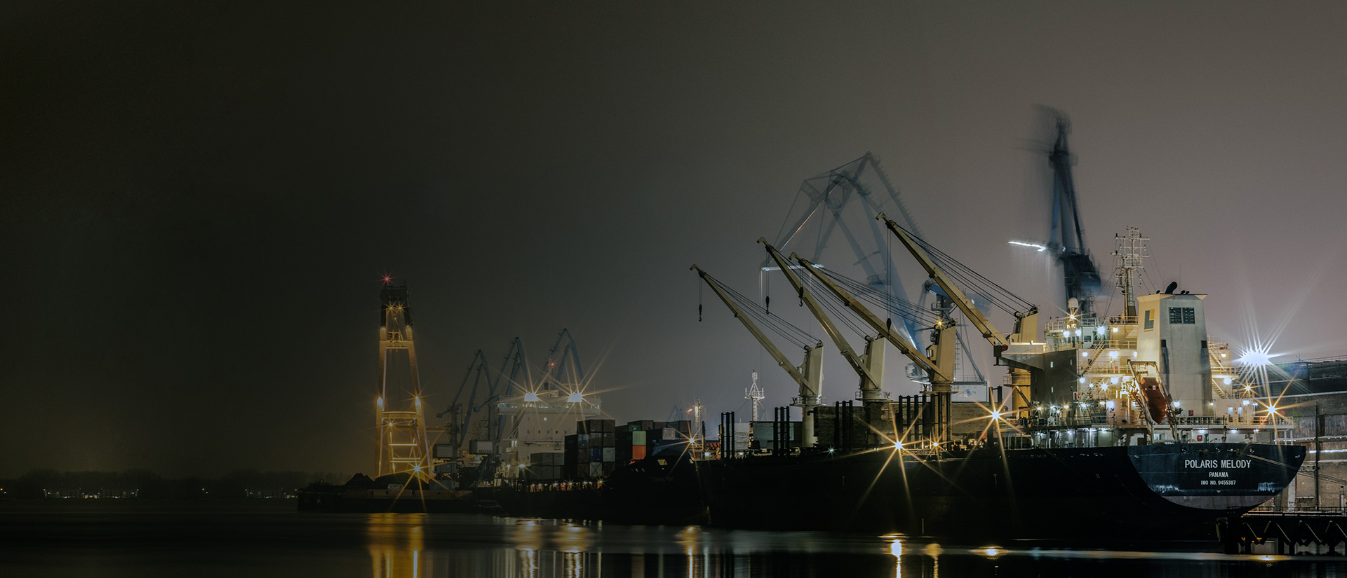 Cargo vessel being loaded by cranes at an international shipping port at dusk